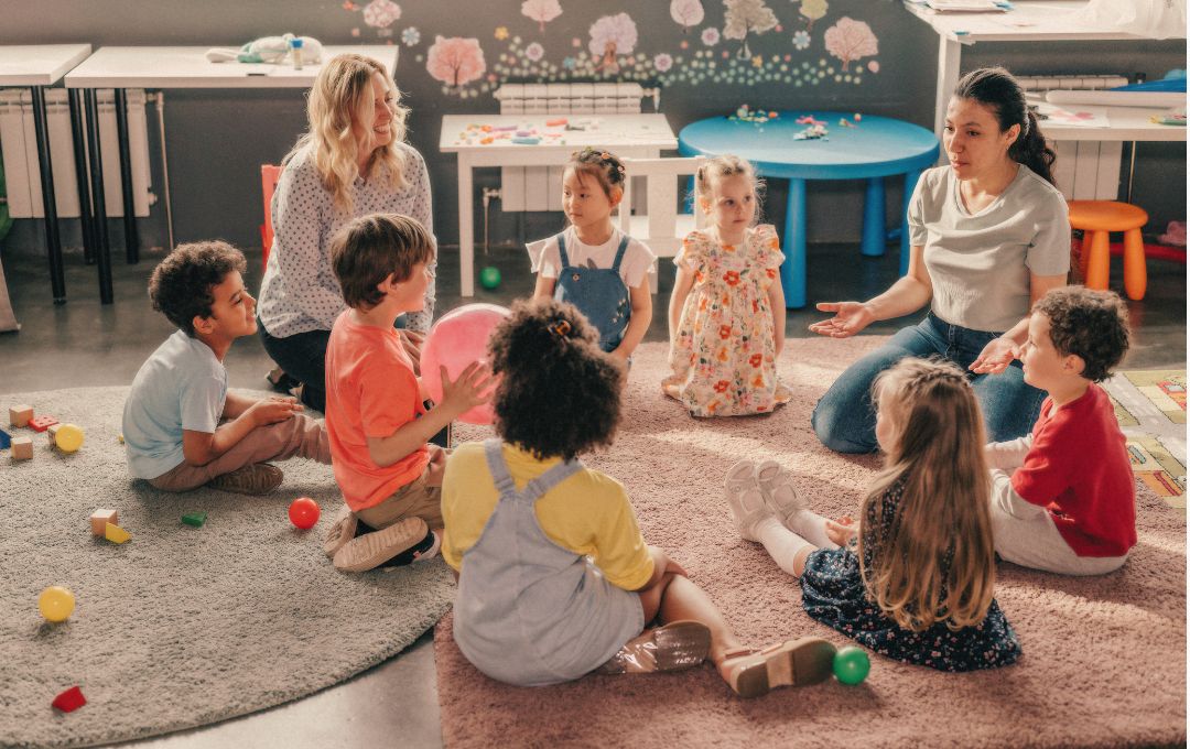 Two teachers sitting with a group of young children on a classroom floor, representing childcare centres