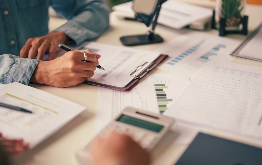 Hands reviewing financial reports, charts, and calculations in a business meeting setting.
